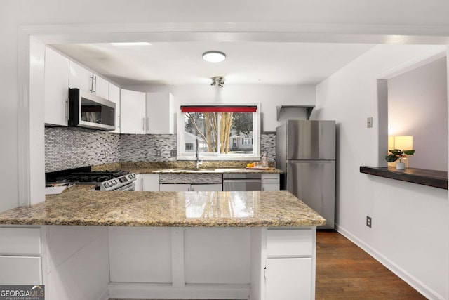 kitchen featuring dark wood-style floors, stainless steel appliances, backsplash, white cabinetry, and a peninsula