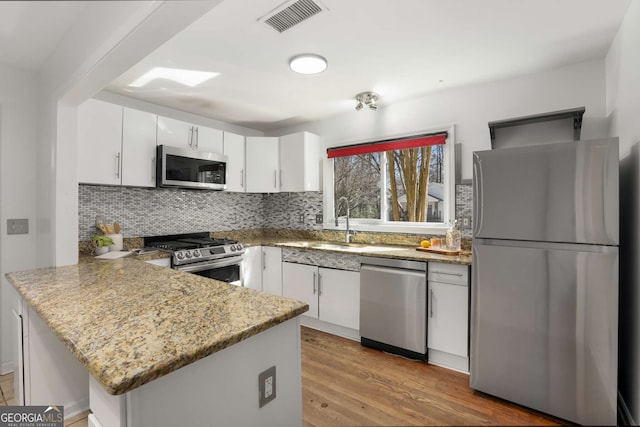 kitchen featuring light wood finished floors, visible vents, backsplash, appliances with stainless steel finishes, and a peninsula