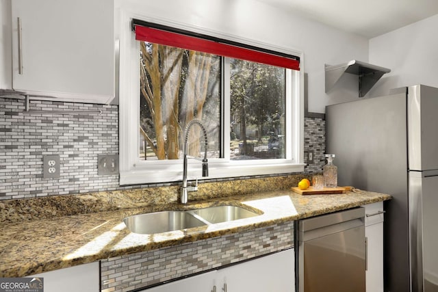 kitchen with white cabinets, light stone counters, a sink, stainless steel appliances, and backsplash