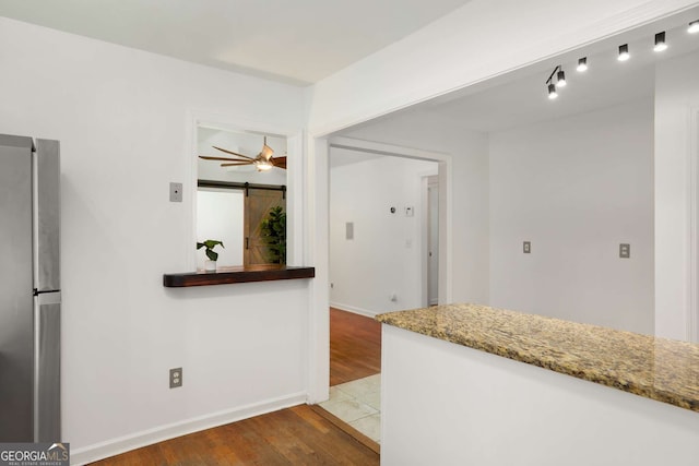 kitchen featuring baseboards, ceiling fan, wood finished floors, freestanding refrigerator, and light stone countertops