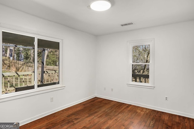 empty room with a healthy amount of sunlight, hardwood / wood-style flooring, visible vents, and baseboards