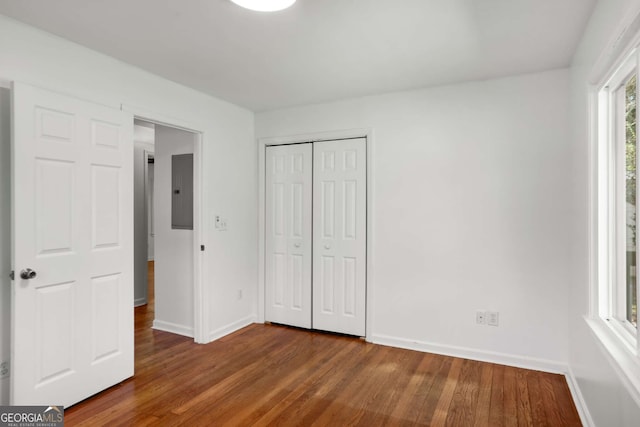 unfurnished bedroom with a closet, electric panel, dark wood finished floors, and baseboards