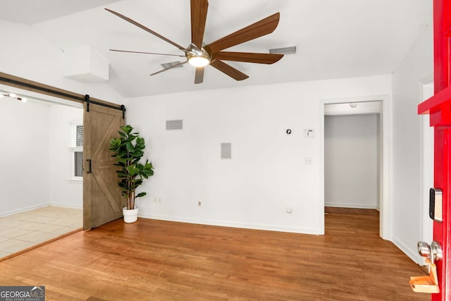 interior space featuring a ceiling fan, wood finished floors, visible vents, and a barn door