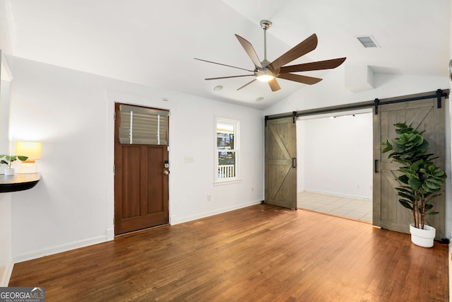 entryway featuring wood finished floors, visible vents, vaulted ceiling, and a barn door