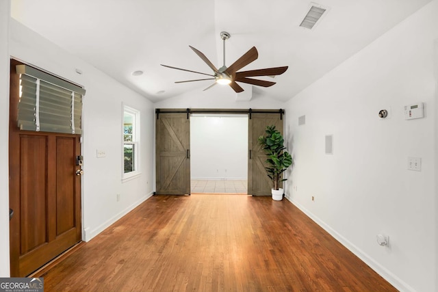 interior space with a barn door, visible vents, ceiling fan, wood finished floors, and vaulted ceiling