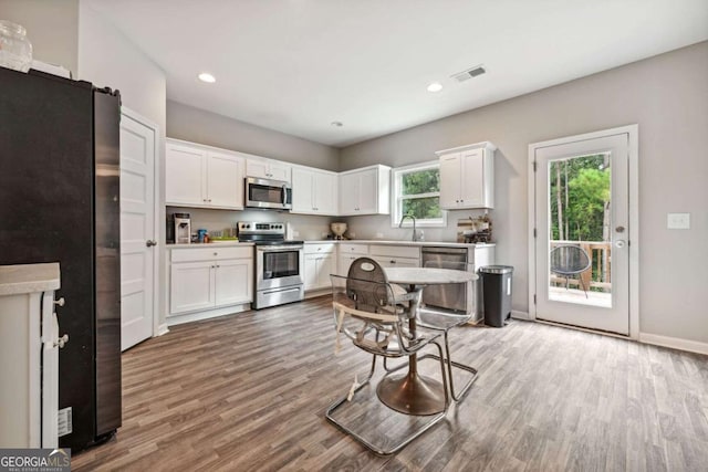 kitchen with light wood finished floors, stainless steel appliances, visible vents, white cabinets, and a sink