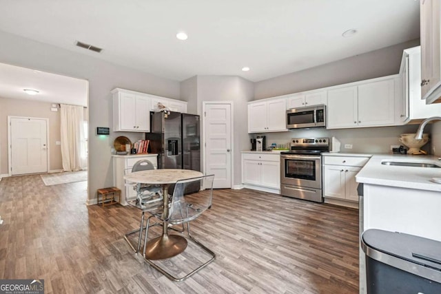 kitchen with stainless steel appliances, wood finished floors, a sink, white cabinets, and light countertops