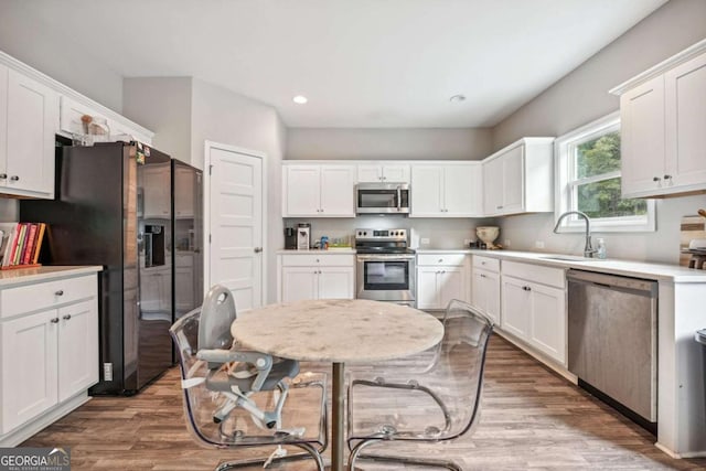 kitchen with white cabinets, stainless steel appliances, a sink, and wood finished floors