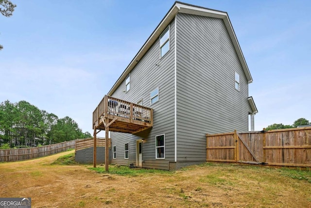 rear view of property featuring fence, a wooden deck, and a lawn