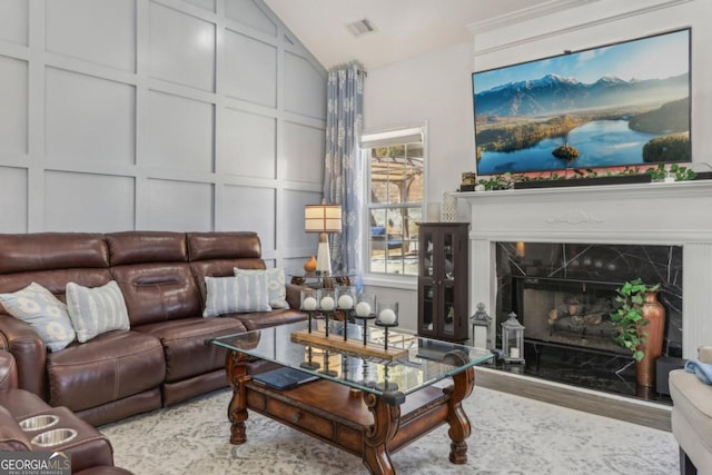 living area with lofted ceiling, a decorative wall, a premium fireplace, wood finished floors, and visible vents