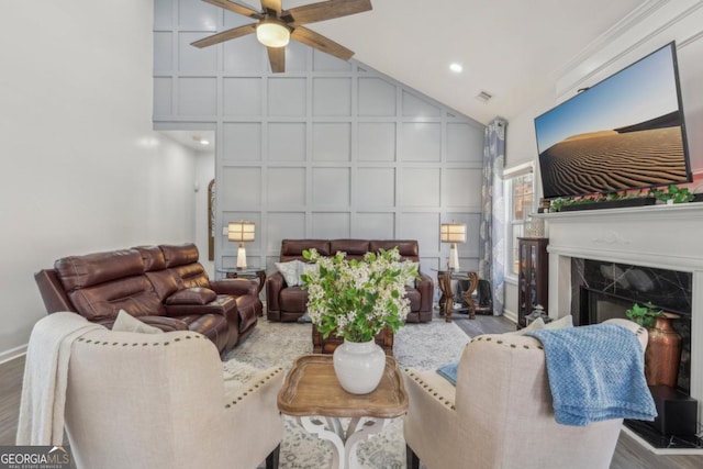 living room with a premium fireplace, a ceiling fan, a decorative wall, and wood finished floors