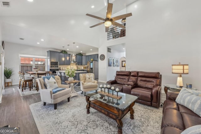 living room with visible vents, a ceiling fan, a towering ceiling, wood finished floors, and recessed lighting