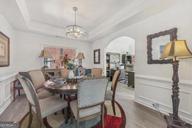 dining room with a tray ceiling, wainscoting, arched walkways, and wood finished floors