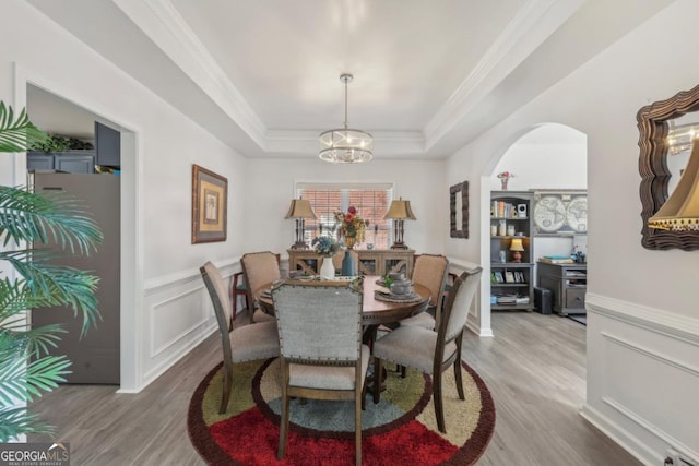 dining room with a decorative wall, wood finished floors, ornamental molding, wainscoting, and a tray ceiling