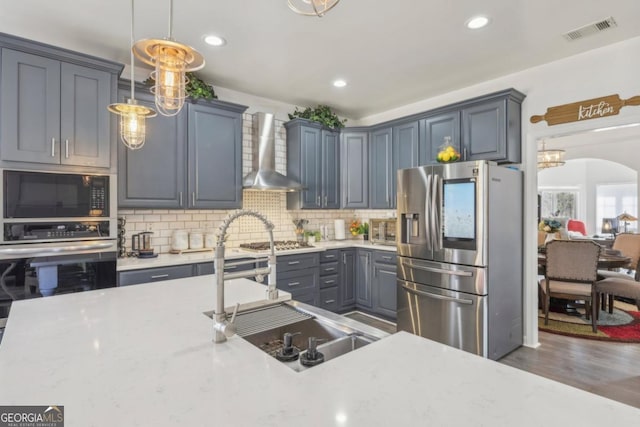 kitchen with arched walkways, stainless steel appliances, decorative backsplash, a sink, and wall chimney exhaust hood