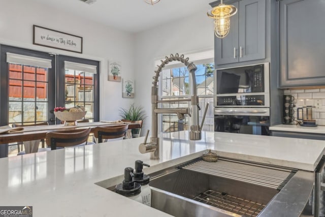 kitchen with backsplash, stainless steel oven, light countertops, black microwave, and a sink