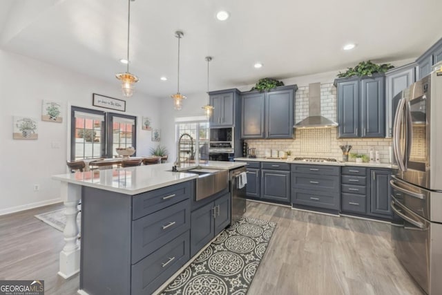 kitchen with a sink, light countertops, wall chimney range hood, appliances with stainless steel finishes, and tasteful backsplash