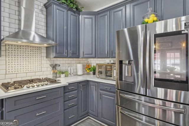 kitchen with a toaster, stainless steel appliances, light countertops, decorative backsplash, and wall chimney exhaust hood