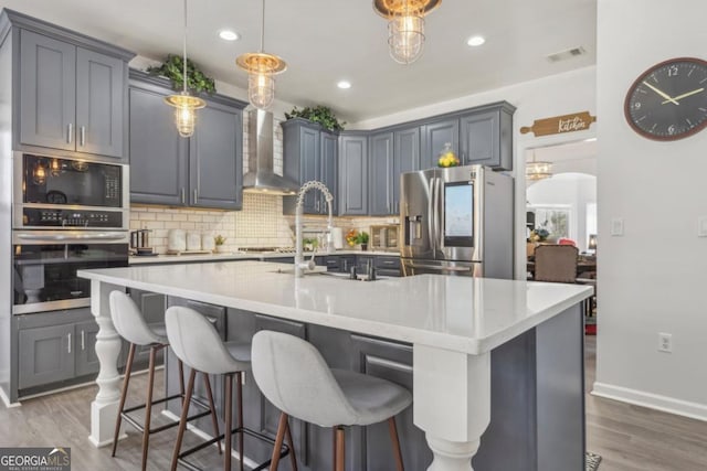 kitchen with stainless steel appliances, wood finished floors, visible vents, wall chimney exhaust hood, and tasteful backsplash