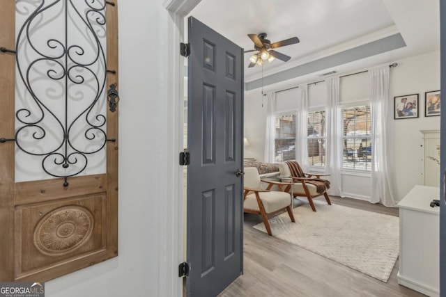 interior space featuring light wood-style floors, a raised ceiling, crown molding, and a ceiling fan