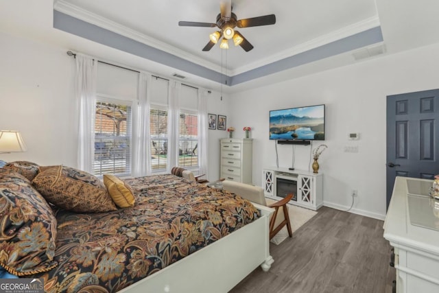 bedroom with a tray ceiling, visible vents, ornamental molding, wood finished floors, and baseboards