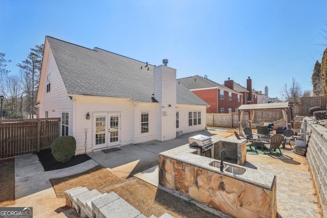 back of house with a patio, a fenced backyard, a chimney, french doors, and a sink