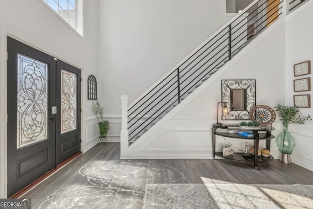 foyer entrance featuring stairs, a decorative wall, wood finished floors, and french doors