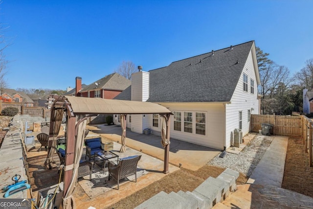 back of property with a patio, a shingled roof, a chimney, and a fenced backyard