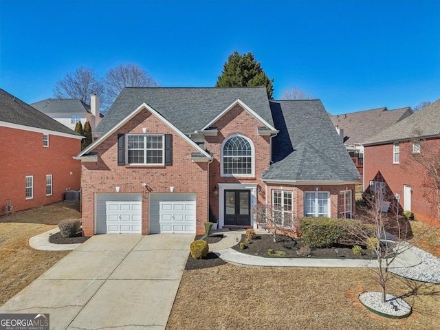 traditional-style house with french doors, brick siding, driveway, and an attached garage