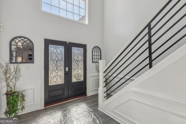 entrance foyer featuring french doors, a wainscoted wall, a decorative wall, wood finished floors, and stairs