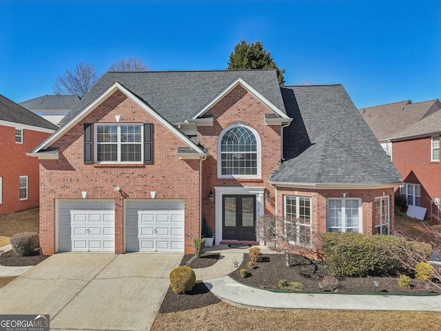 traditional home featuring driveway, brick siding, an attached garage, and french doors