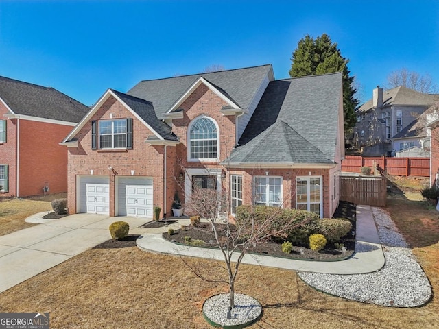 traditional-style home featuring a garage, concrete driveway, roof with shingles, fence, and brick siding