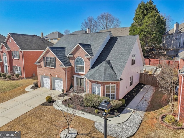 traditional-style house with an attached garage, brick siding, a shingled roof, fence, and driveway