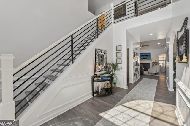 entrance foyer with a fireplace, a towering ceiling, ceiling fan, wood finished floors, and stairs