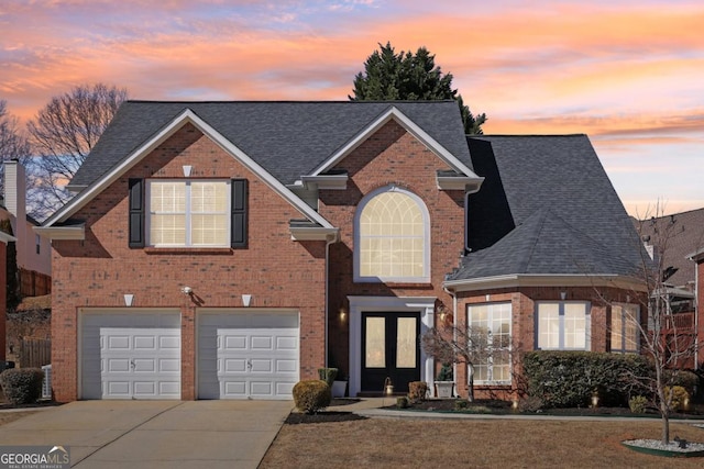 traditional home featuring an attached garage, brick siding, a shingled roof, driveway, and french doors