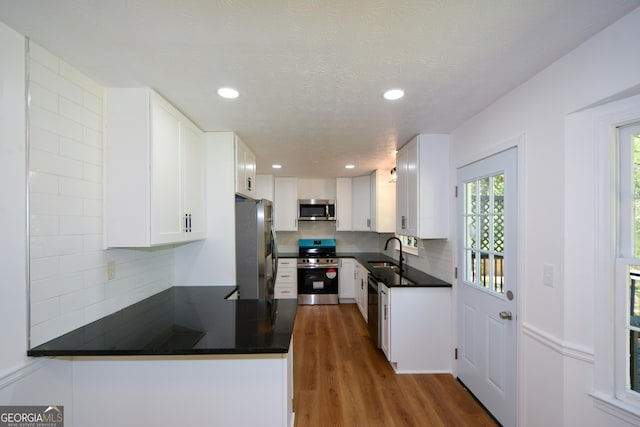 kitchen with appliances with stainless steel finishes, a sink, dark countertops, and backsplash