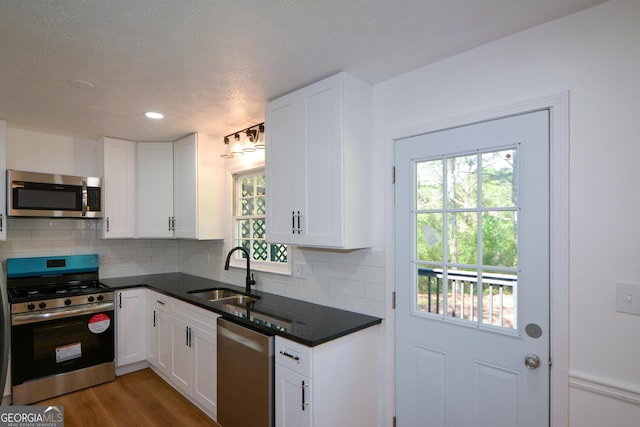 kitchen featuring white cabinetry, dark countertops, decorative backsplash, stainless steel appliances, and a sink