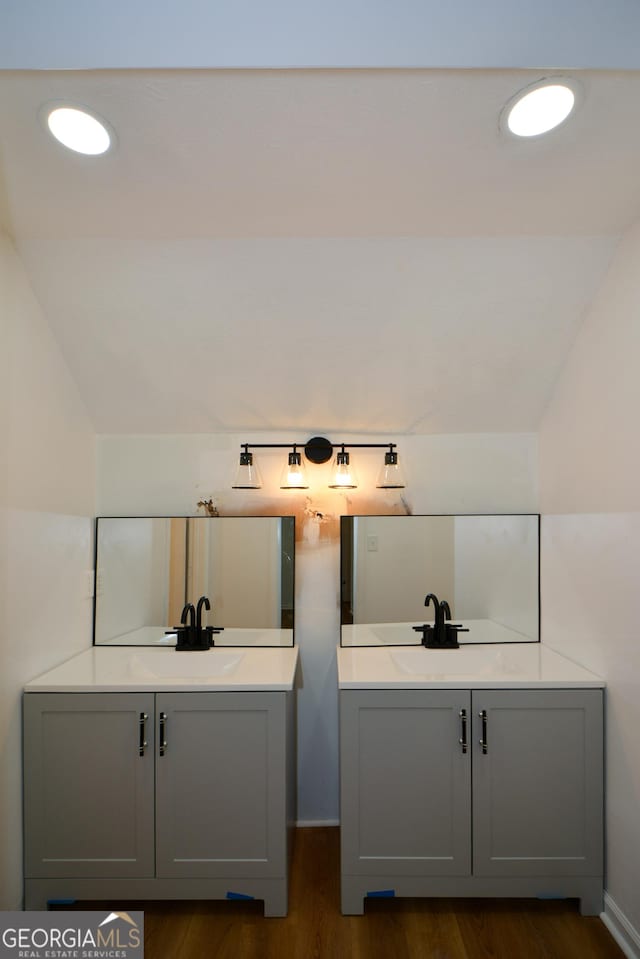 bathroom with two vanities, vaulted ceiling, a sink, and wood finished floors
