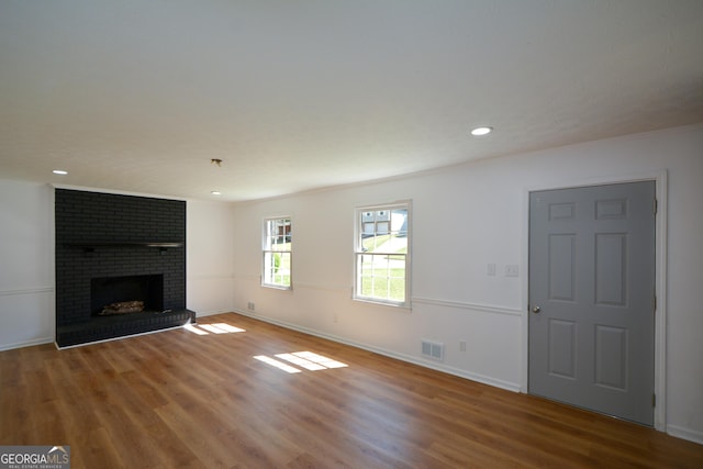 unfurnished living room featuring visible vents, a brick fireplace, wood finished floors, and baseboards