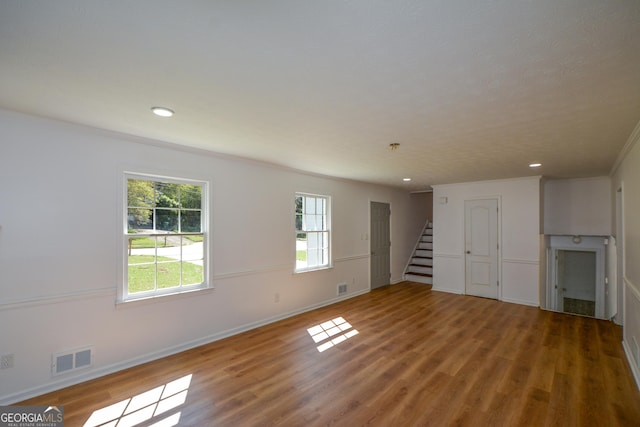 unfurnished living room featuring visible vents, baseboards, ornamental molding, wood finished floors, and stairs