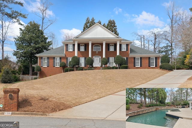 greek revival house with a shingled roof, brick siding, and an outdoor pool