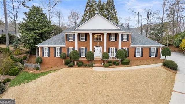 greek revival inspired property with driveway, brick siding, and roof with shingles