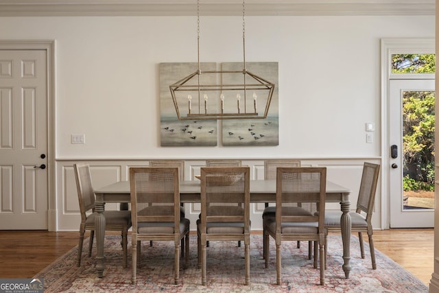 dining area with a wainscoted wall, an inviting chandelier, wood finished floors, and a decorative wall