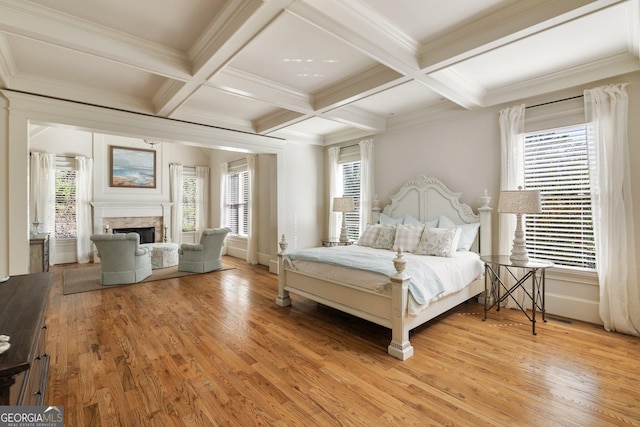 bedroom featuring beamed ceiling, multiple windows, a fireplace, and light wood finished floors