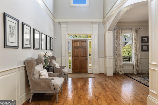 entrance foyer with crown molding, a wainscoted wall, wood finished floors, arched walkways, and a decorative wall