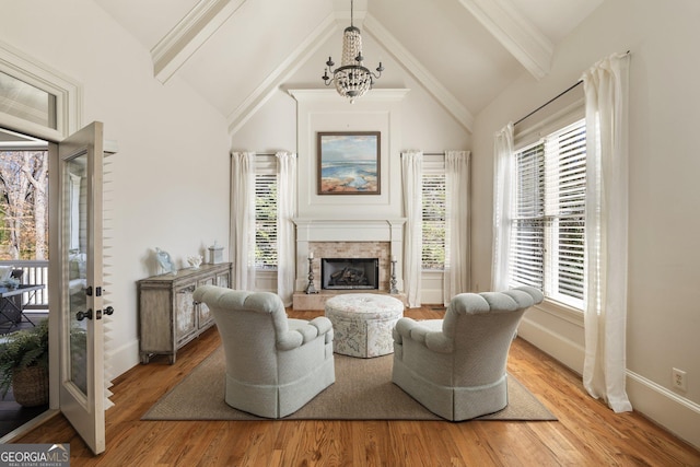 living area with baseboards, light wood finished floors, beam ceiling, a fireplace with raised hearth, and a chandelier