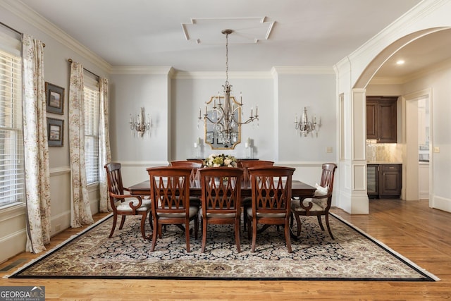 dining area featuring arched walkways, ornamental molding, an inviting chandelier, and wood finished floors