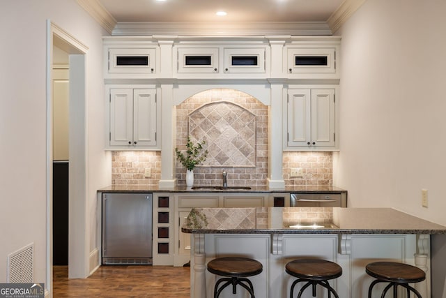 kitchen with visible vents, a breakfast bar, dark wood finished floors, a sink, and crown molding