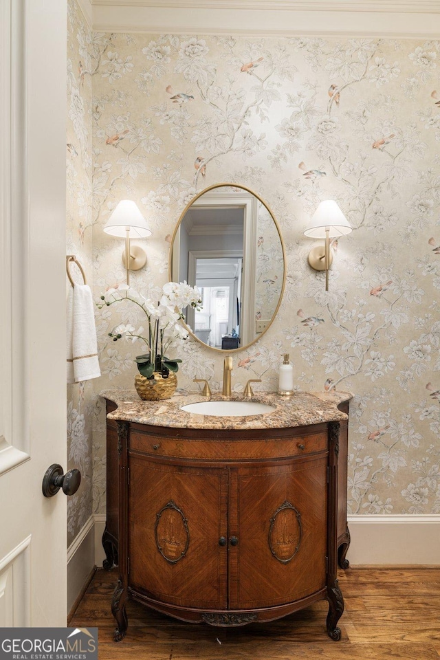 bathroom with wallpapered walls, vanity, baseboards, and wood finished floors