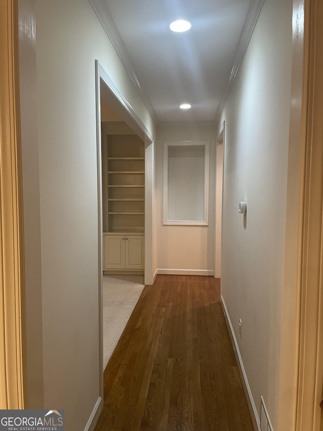 hall with built in features, dark wood finished floors, crown molding, visible vents, and baseboards